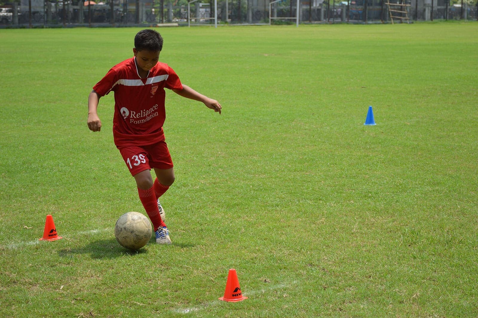 Under-14 boy in a red kit dribbles a football through cones during grassroots training in Kolkata