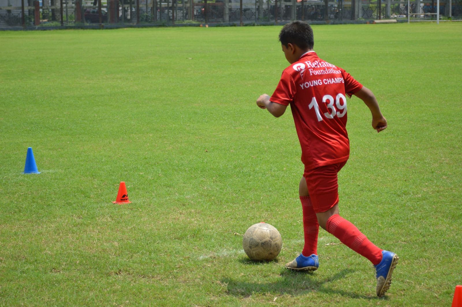 Under-14 boy in a red kit dribbles a football during grassroots training in Kolkata