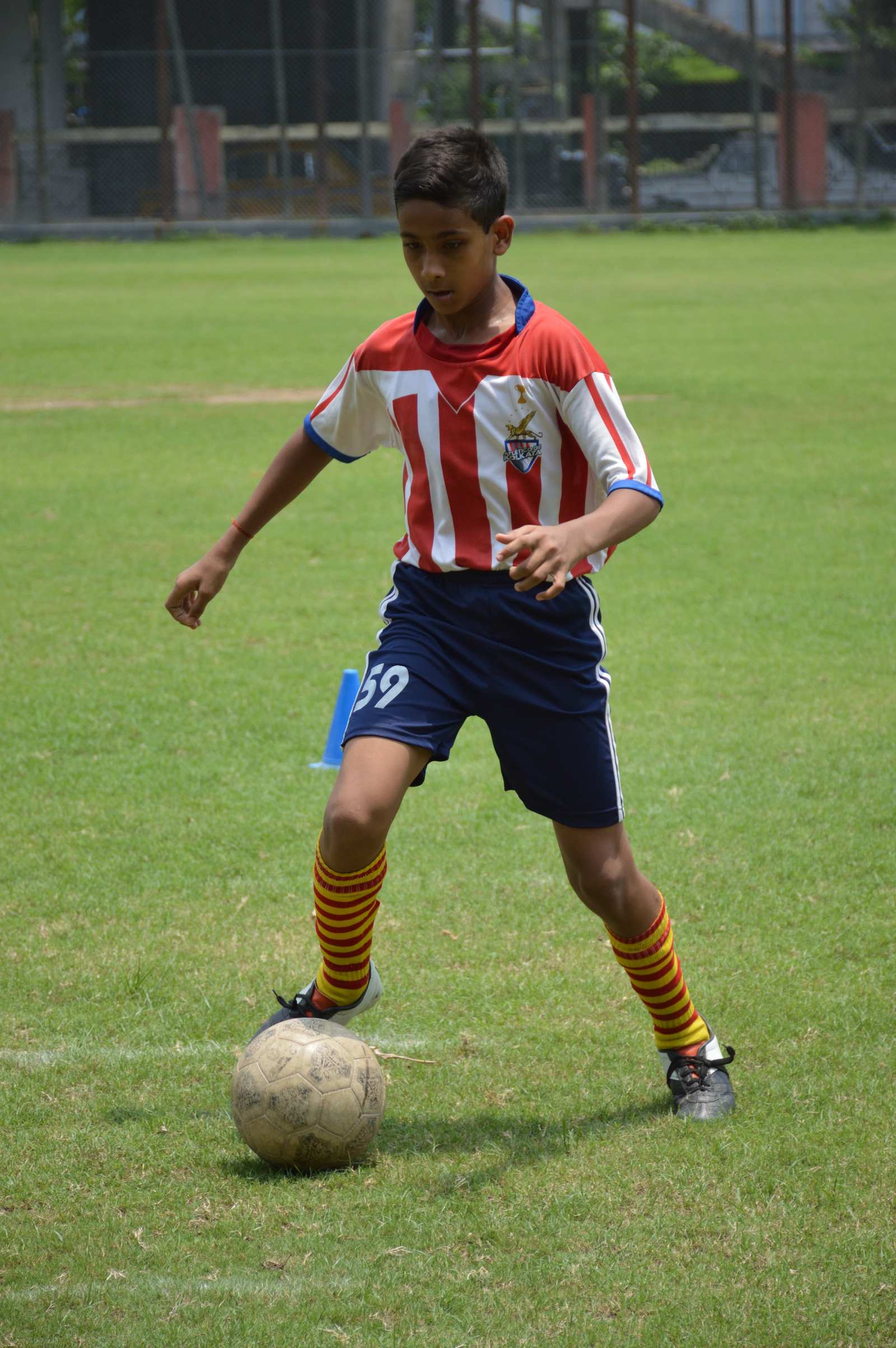 Under-14 boy in a red-and-white kit dribbles a football during grassroots training in Kolkata
