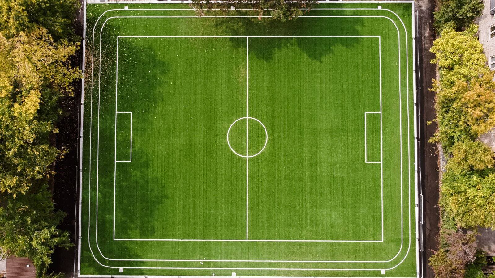 Top‑down view of green football field surrounded by trees