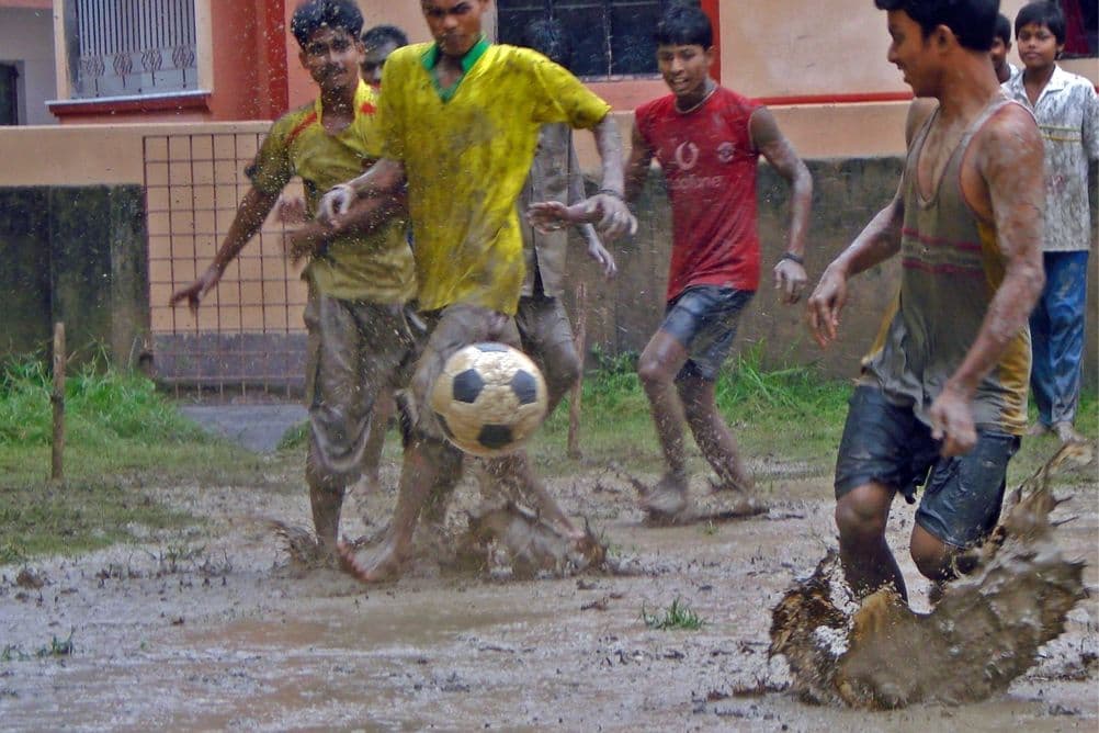 Boys play street football in the mud in Kolkata, with the ball in mid-air