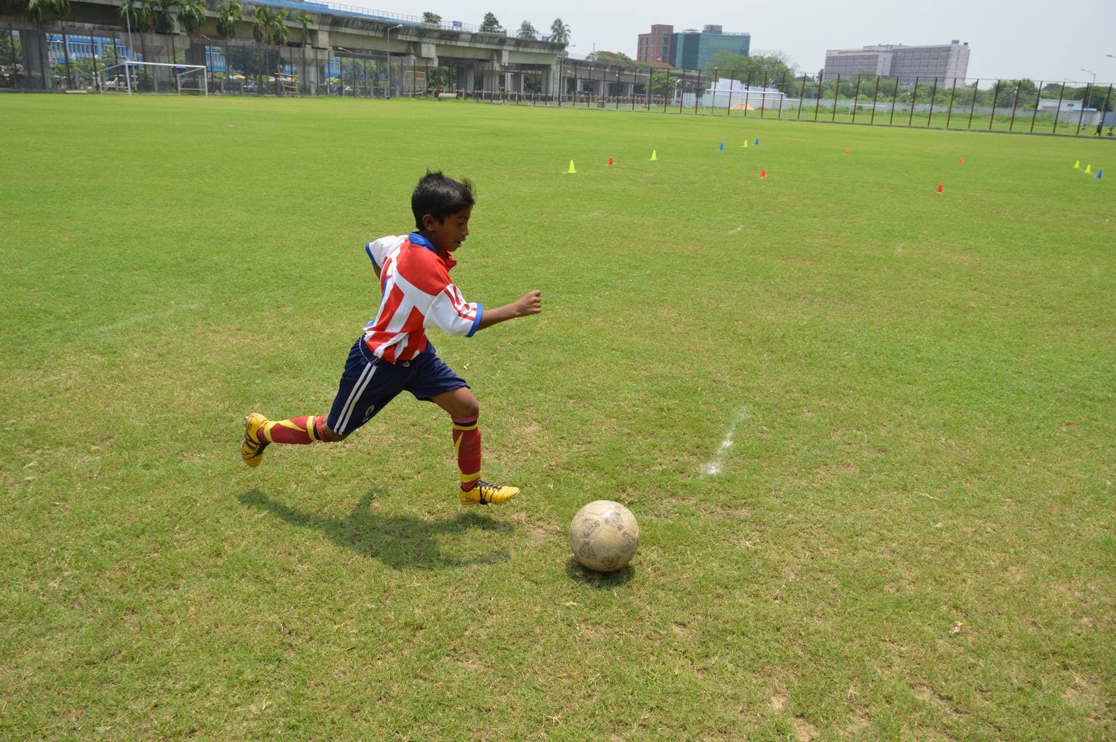 Young footballer in kit dribbling a ball during grassroots training on a Kolkata ground