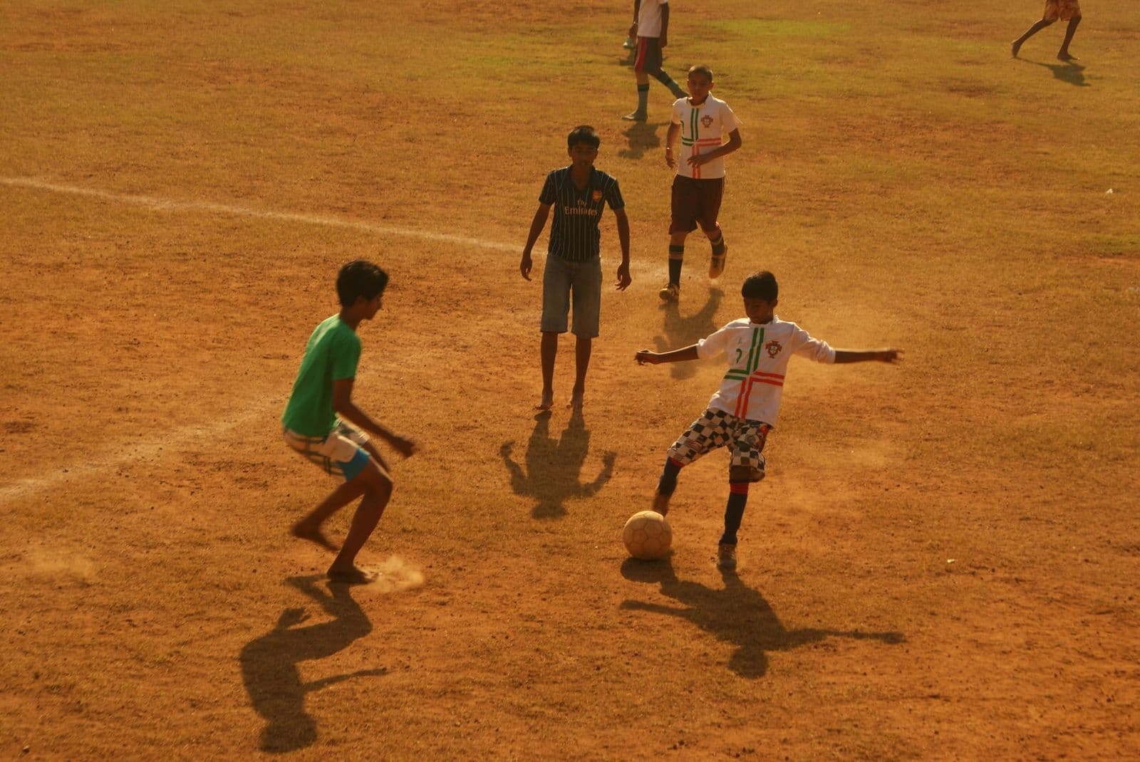 Boys contest a football on a dusty Indian ground