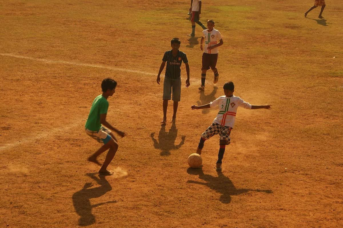 Indian boys dribbling a football on a dusty pitch